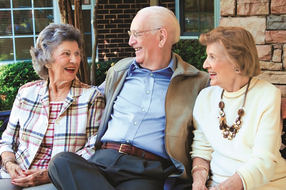 Three elderly friends enjoy a lively conversation outside.