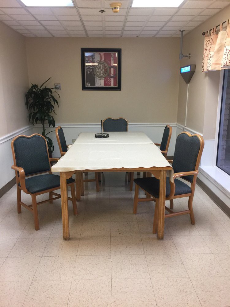A simple dining area with a table and six chairs, decorated with a plant and wall art.