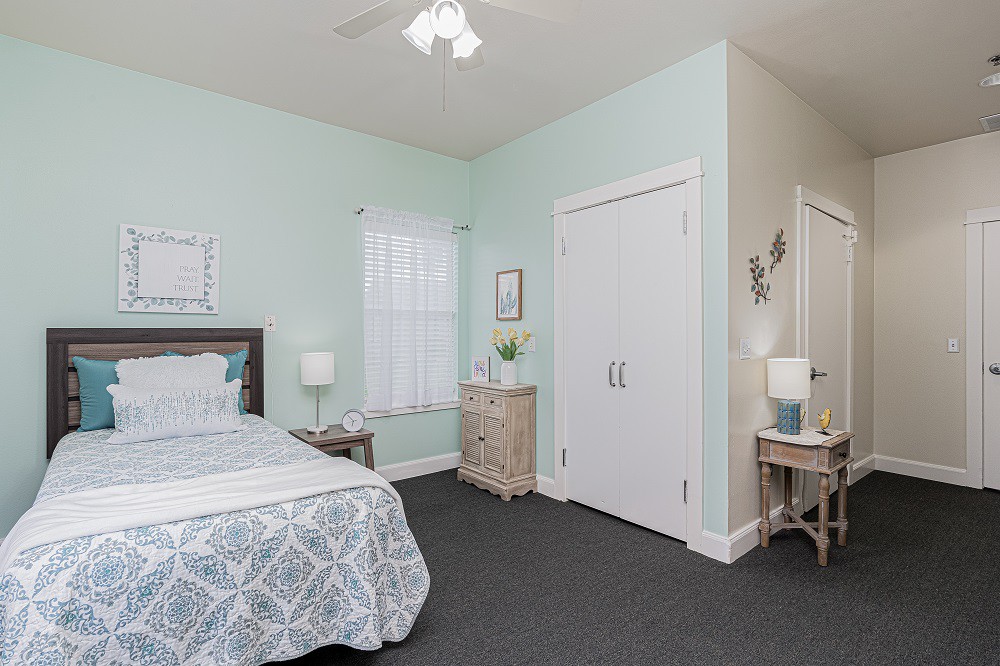 A cozy bedroom with pastel walls, featuring a bed, nightstands with lamps, and a closet.