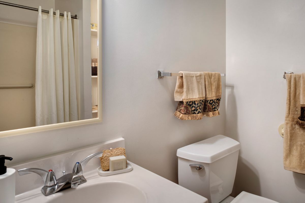 A clean and neatly organized bathroom with a mirror, sink, toilet, and towels.