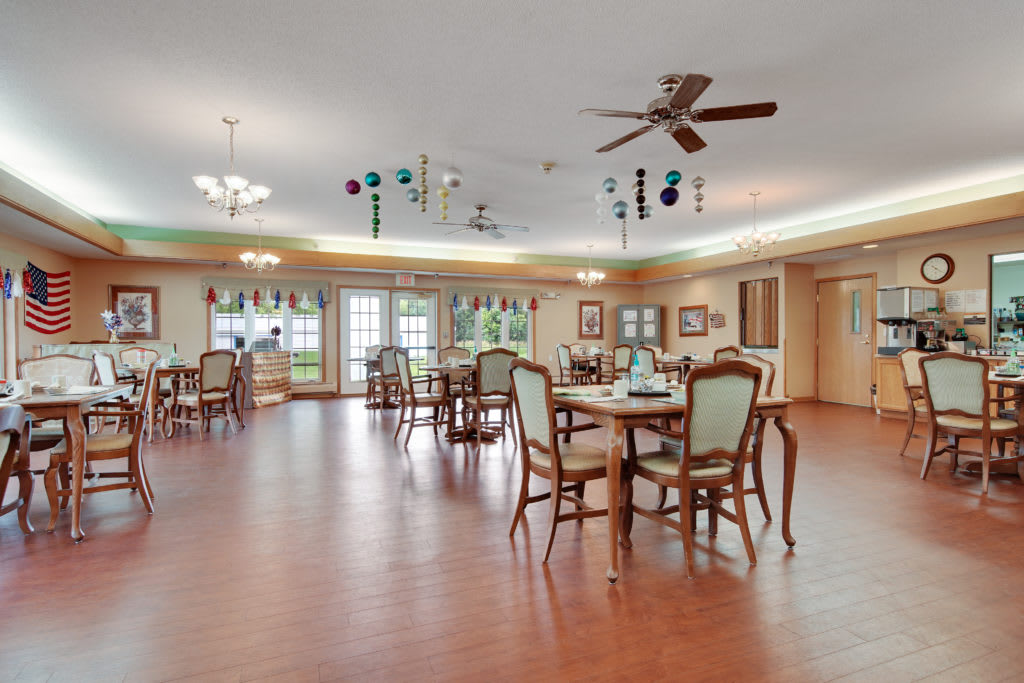 A spacious dining area with wooden floors, elegantly arranged tables and chairs, ceiling fans, and decorative lighting.