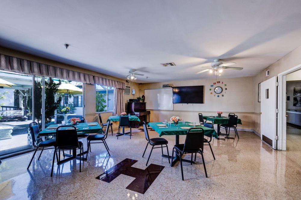 A bright dining area with several tables and chairs, lit by natural light through large windows.