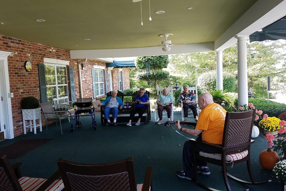 A group of elderly people sitting and conversing on an outdoor porch.