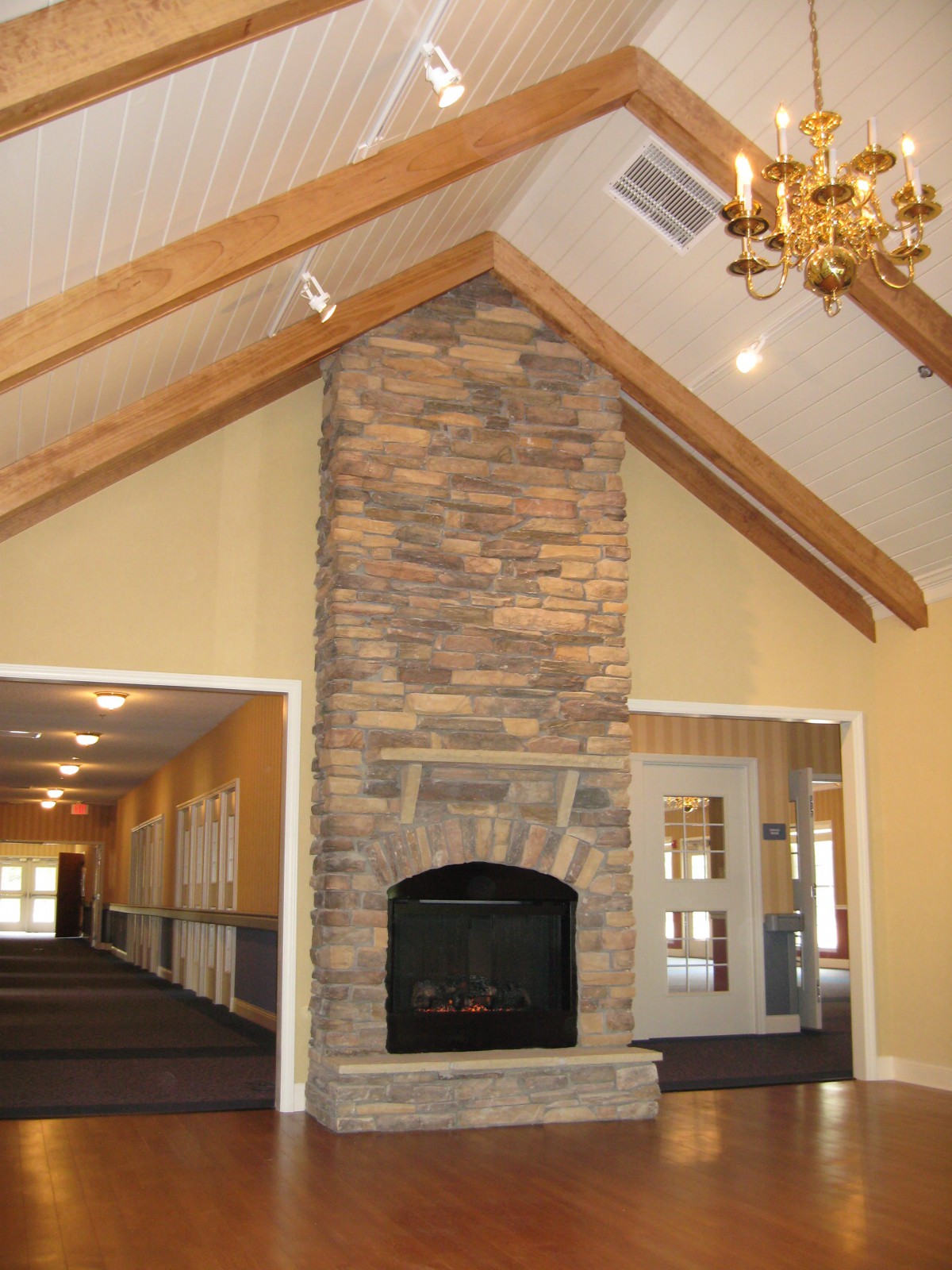 A spacious room with a stone fireplace, vaulted ceiling, and wooden beams.