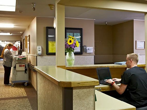 A reception area with a desk, computer, and vase of flowers in a hallway setting.