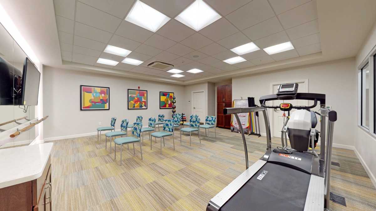 A modern conference room with colorful artwork, rows of chairs, and a treadmill.