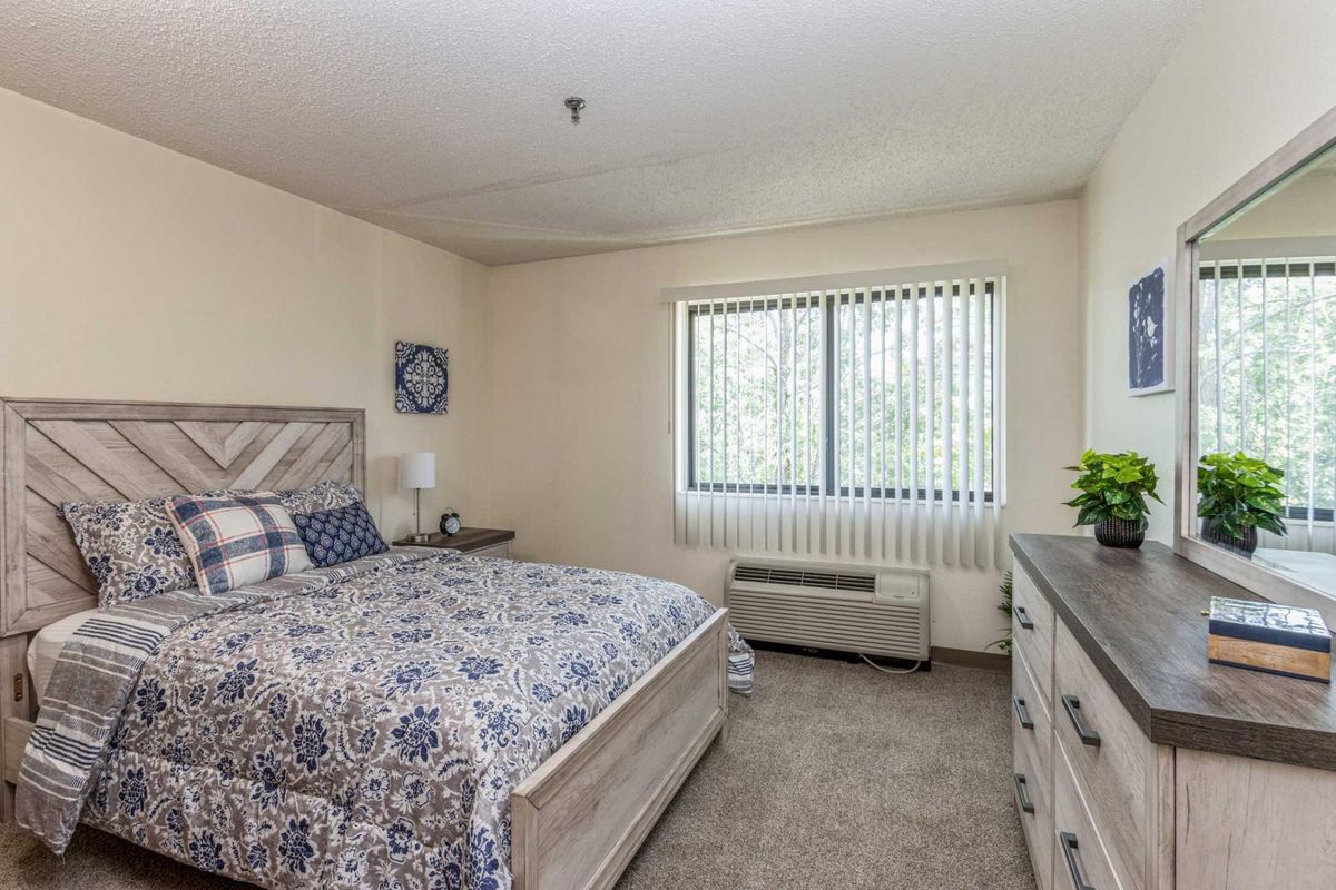 A cozy bedroom with a bed, dresser, and window with vertical blinds.