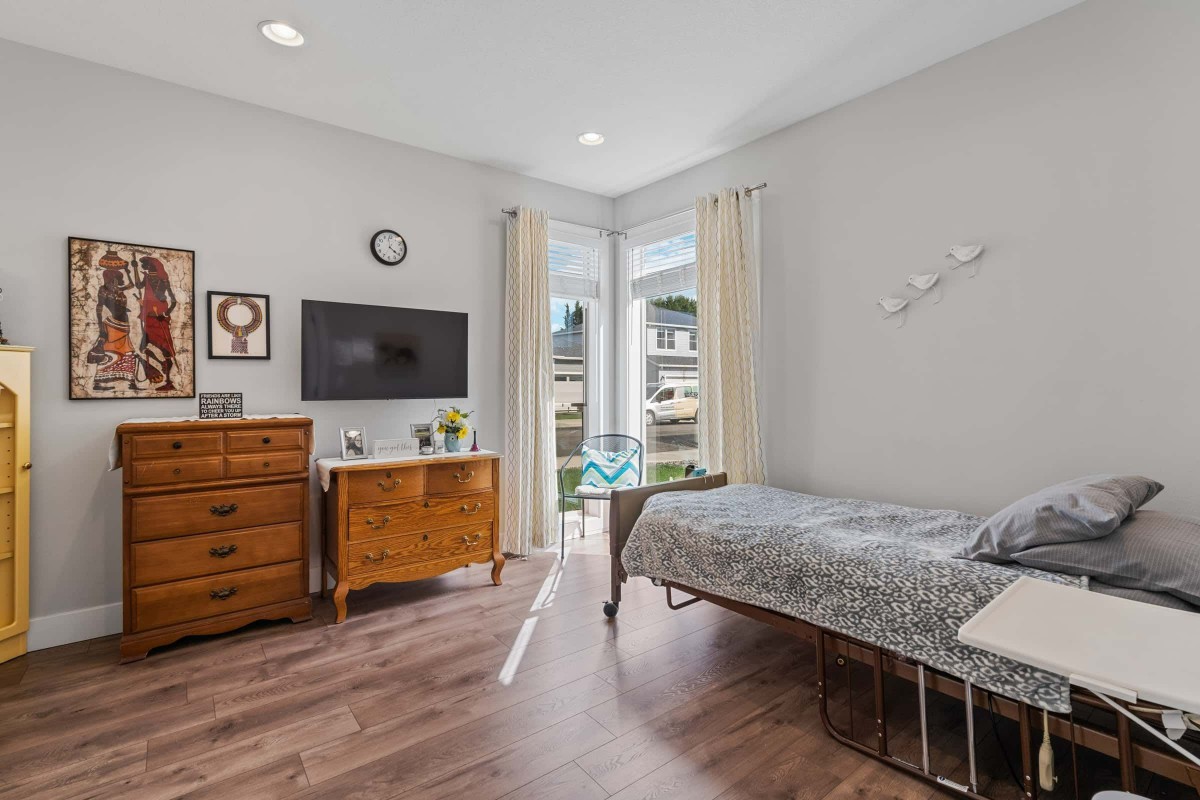 A cozy bedroom with a bed, dresser, and a wall-mounted TV.