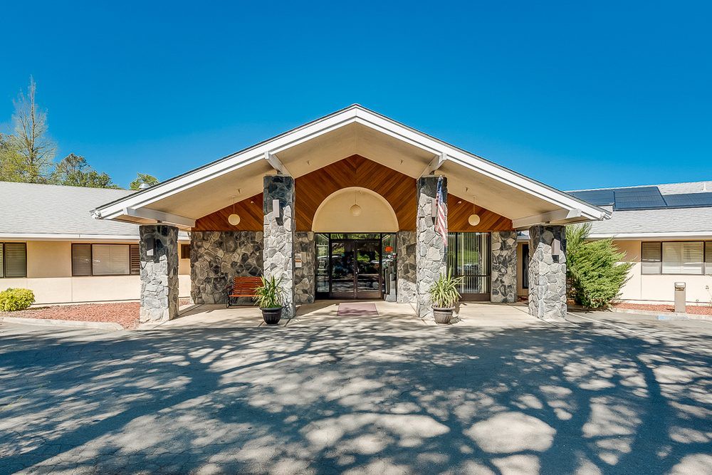 Front entrance of a building with stone columns and a peaked roof on a sunny day.