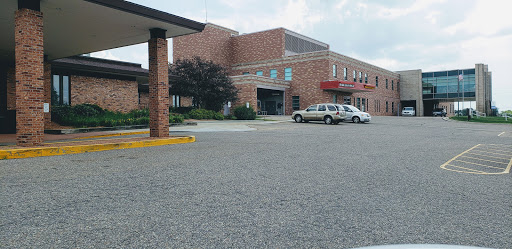A brick hospital building with a parking lot, under a cloudy sky.