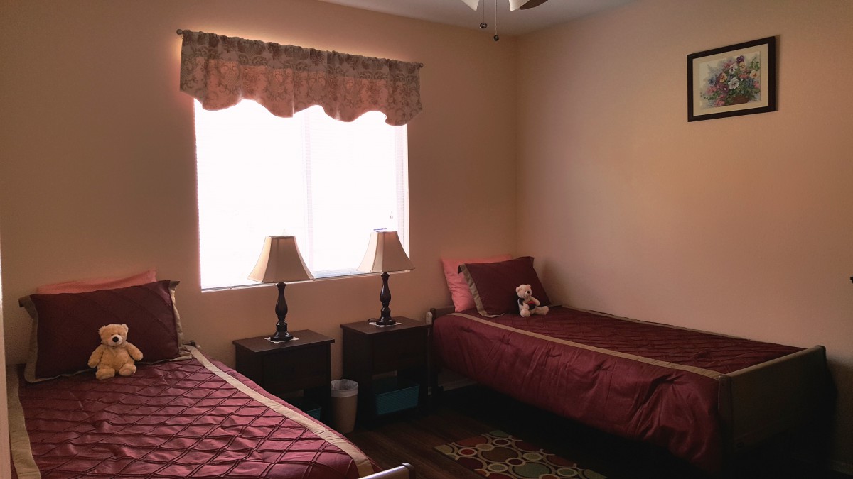A cozy bedroom with two single beds and a teddy bear on one bed, complemented by lamps on nightstands beside a window.