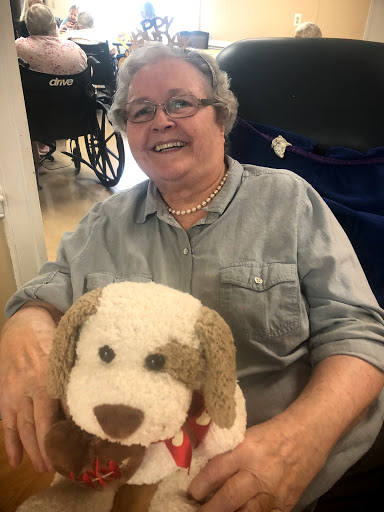 A joyful elderly woman smiles while holding a cute stuffed dog.