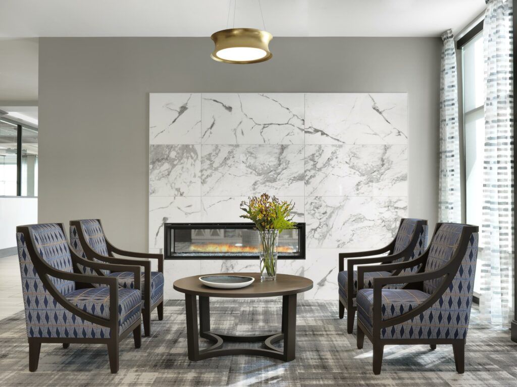 A modern living room with four armchairs arranged around a round coffee table, featuring a marble wall with an integrated fireplace.
