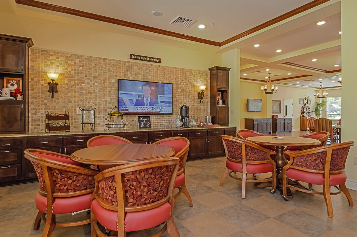 A cozy dining area with wooden tables, red cushioned chairs, a decorative stone wall, and a mounted television.