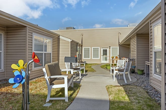 A courtyard with benches and a pathway in a residential area under a partly cloudy sky.