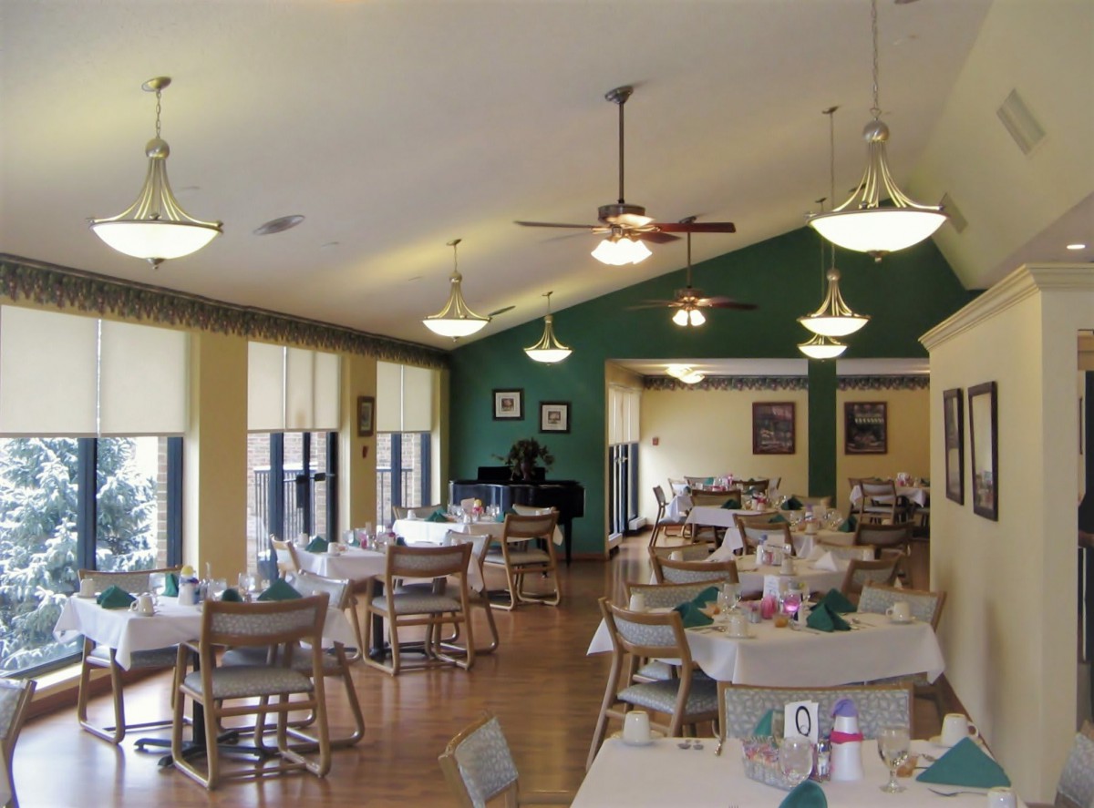 A well-lit dining area with neatly arranged tables and chairs, featuring decorative lighting and large windows.