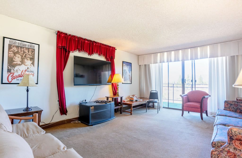 A cozy living room with a large TV, red curtains, and a balcony view.
