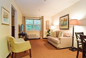 A cozy living room with a sofa, chair, and artwork on the walls, featuring a large window that allows natural light to brighten the space.