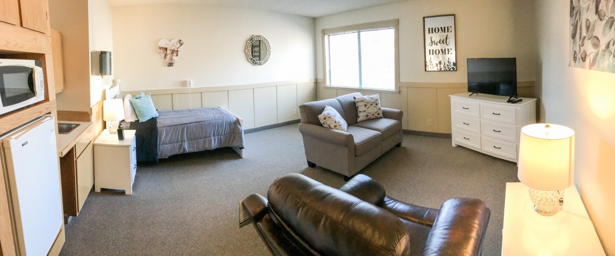 A spacious and cozy room featuring a sofa, bed, and large window.
