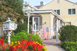 A cozy house with a garden full of vibrant flowers and an American flag by the entrance.
