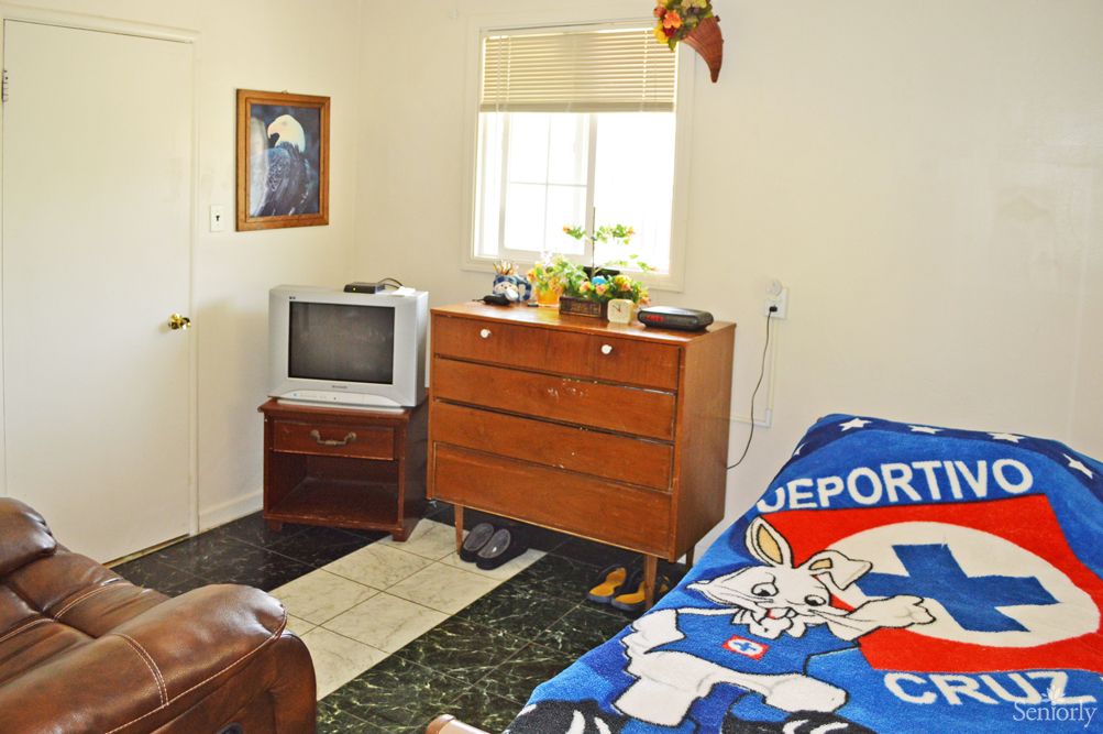 A cozy bedroom with a television, dresser, and a sports-themed blanket.