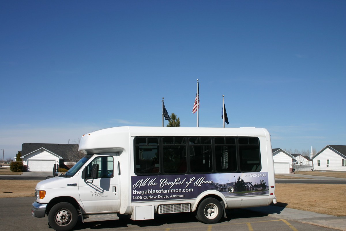 A white shuttle bus parked outdoors with flags flying in the background.