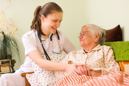 A nurse providing care and support to an elderly woman, both smiling warmly.