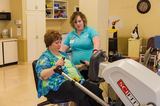 A healthcare professional assists a patient with an exercise machine during a rehabilitation session.