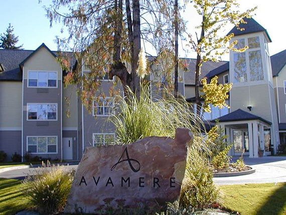 A large stone sign with 'Avamere' in front of a multi-story building surrounded by trees and landscaping.