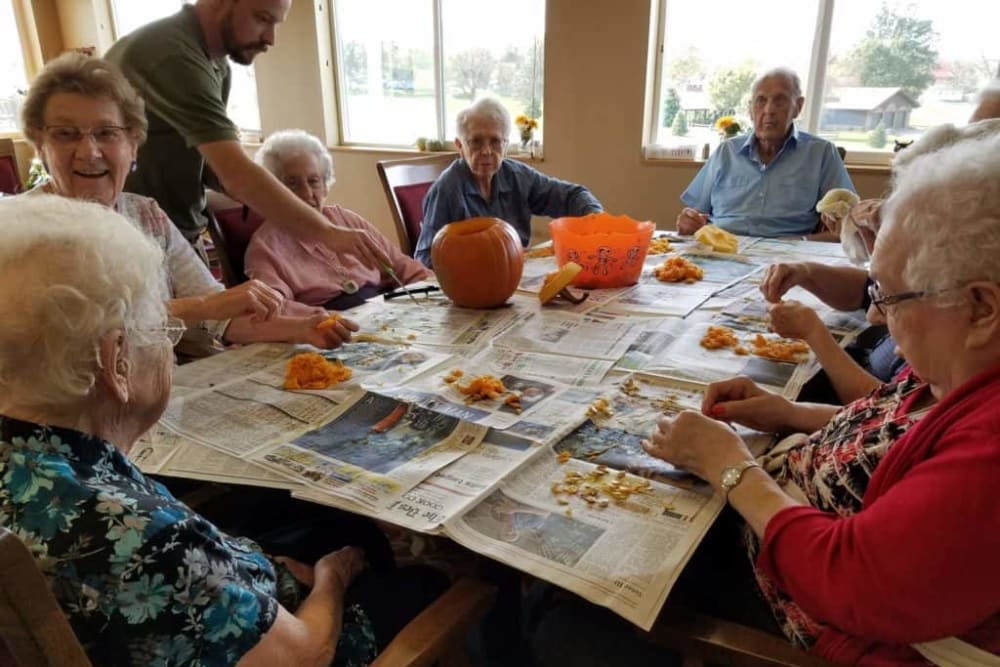 A group of elderly individuals participating in a pumpkin carving activity together indoors.