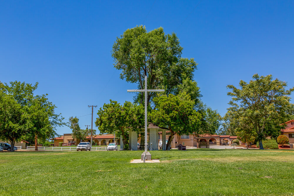 A cross stands prominently in a grassy park area with trees and a clear blue sky.