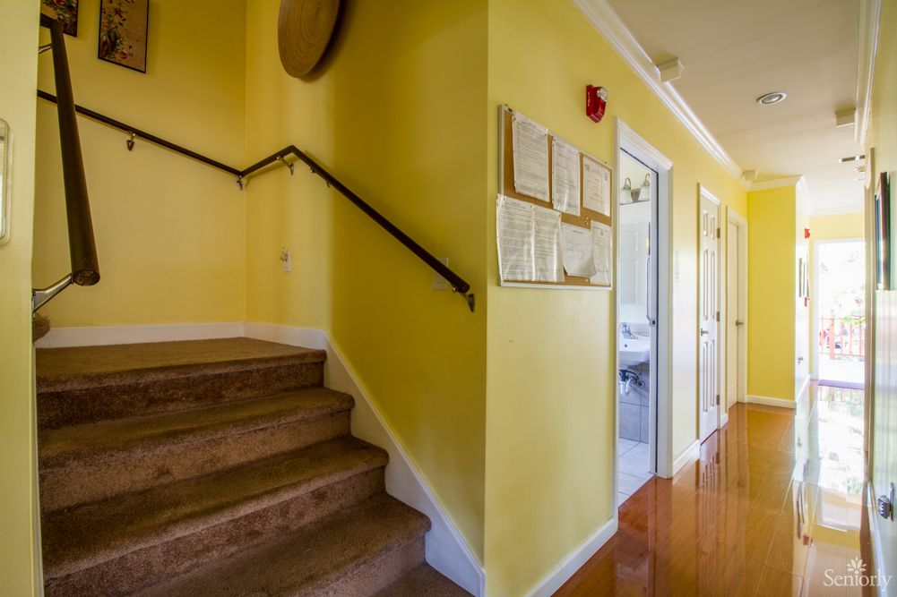 A brightly lit hallway with yellow walls and wooden floors featuring a staircase on the left.