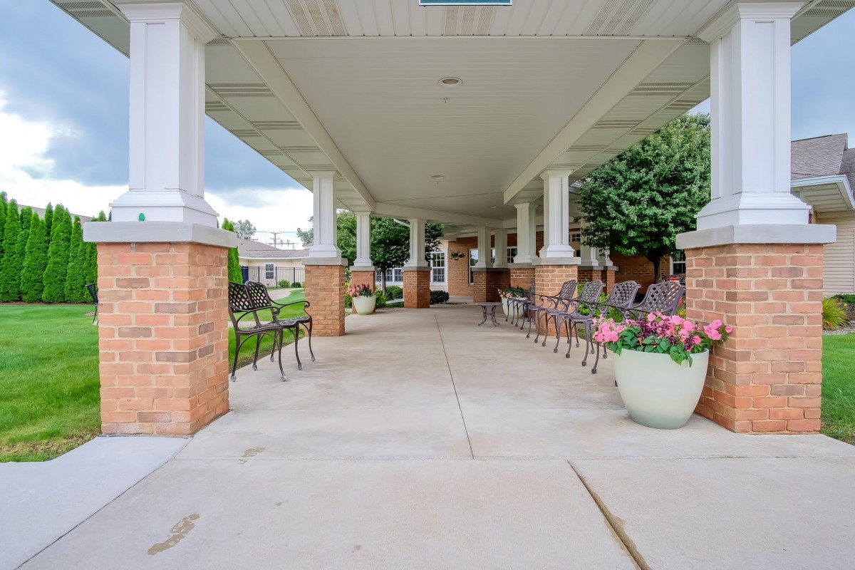 A covered walkway with benches and flower pots leading to a building entrance.