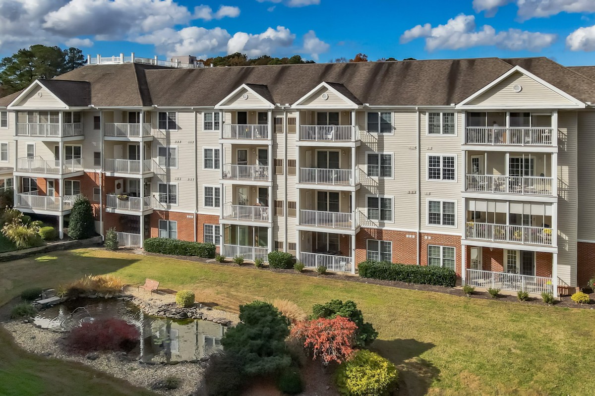 A multi-story apartment building with balconies and well-maintained landscaping under a cloudy sky.