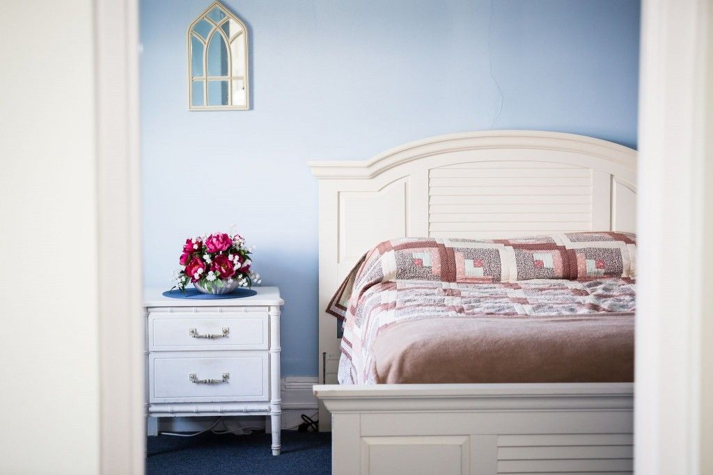 A cozy bedroom featuring a white bed and nightstand with a bouquet of flowers.