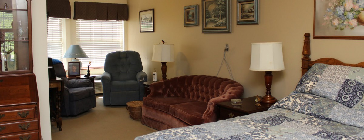A cozy living room with a brown sofa and a blue armchair, featuring lamps and wall art.