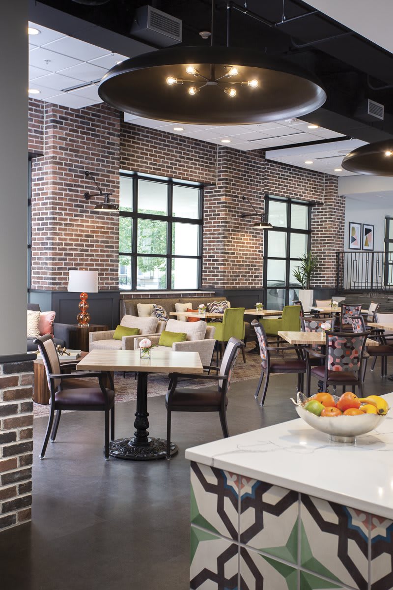 A modern restaurant interior with brick walls, featuring neatly arranged tables and chairs in a well-lit dining area.