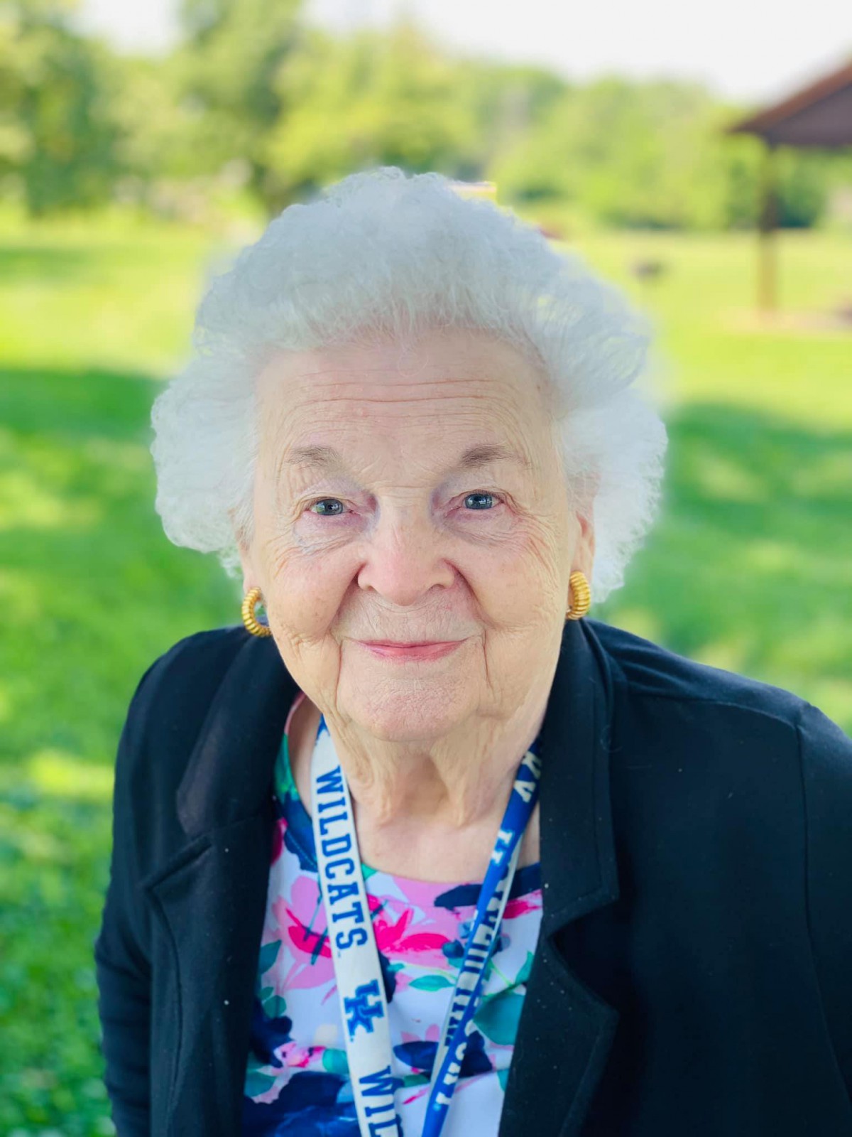 An elderly woman enjoying a sunny day outdoors, surrounded by lush greenery.