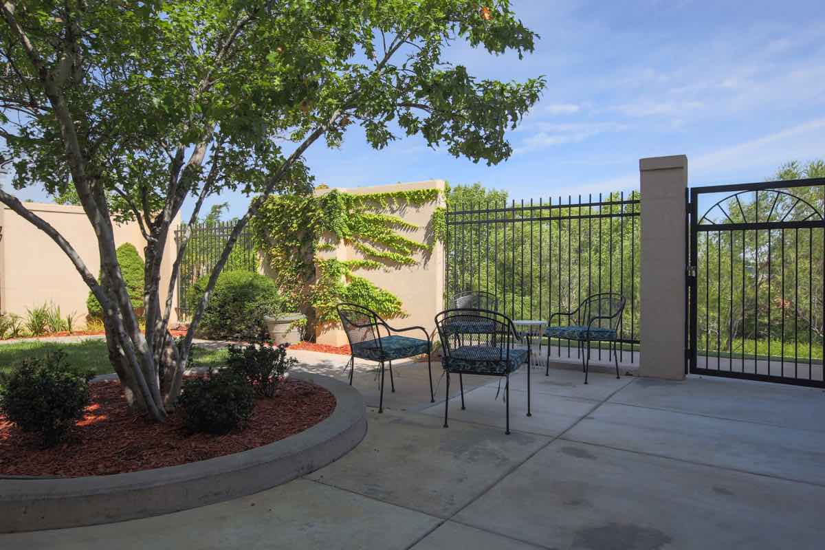 A serene outdoor patio area with chairs and a table surrounded by greenery.