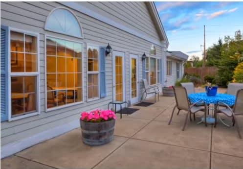 A cozy patio area with outdoor furniture and a flower pot, adjacent to a well-lit house exterior.