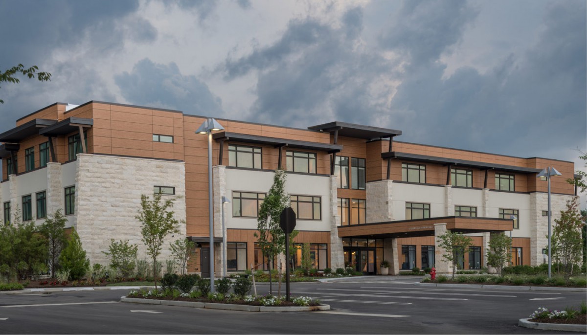 A modern commercial building with a spacious parking lot under a cloudy sky.