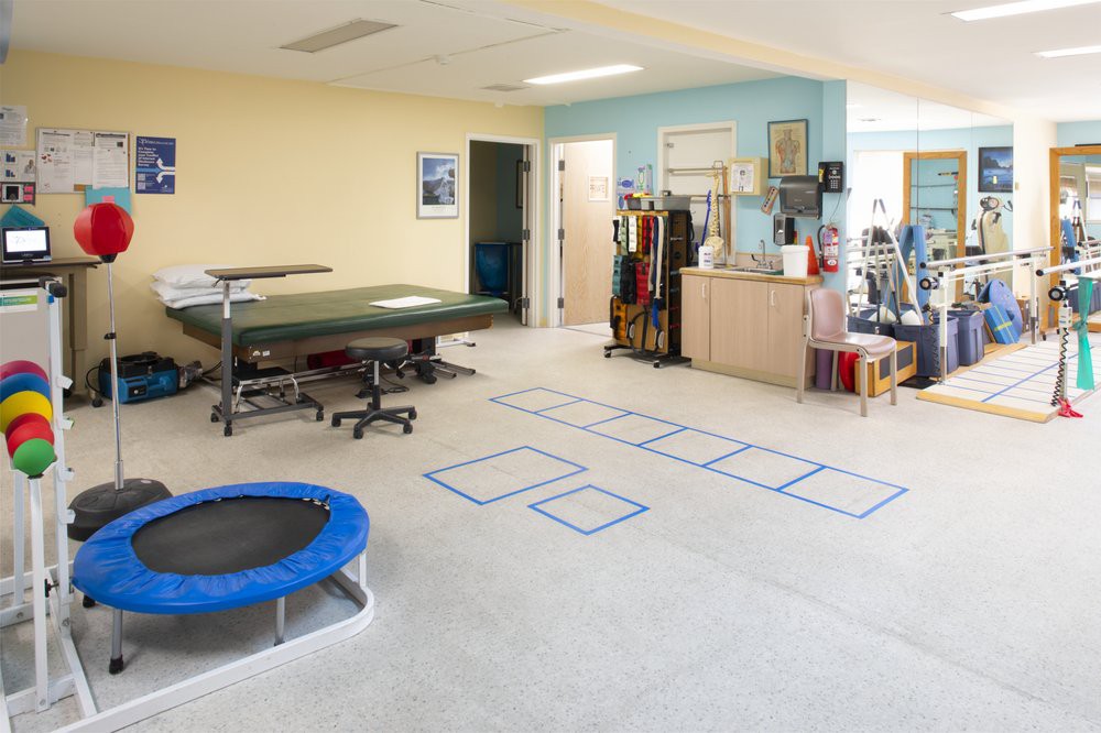 A physical therapy room equipped with various exercise equipment, including a trampoline and mats.