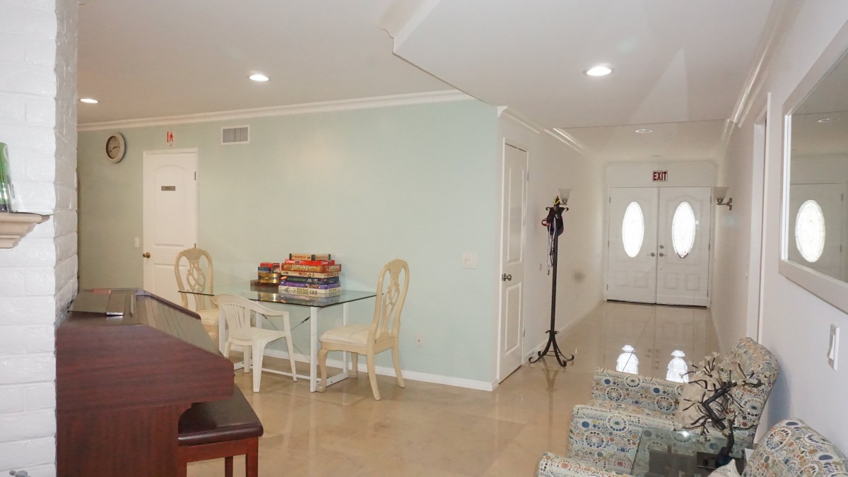 A cozy living and dining area with a glass table, chairs, and a coat rack near the entrance.