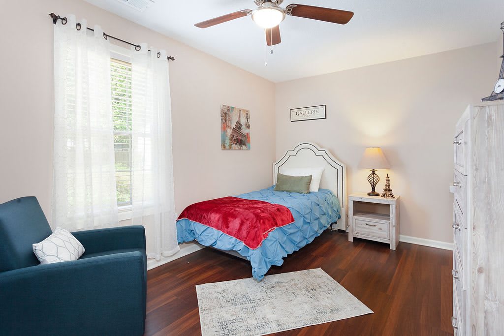 A cozy bedroom with a single bed, decorated in soothing colors, featuring a bedside lamp and artwork on the walls.