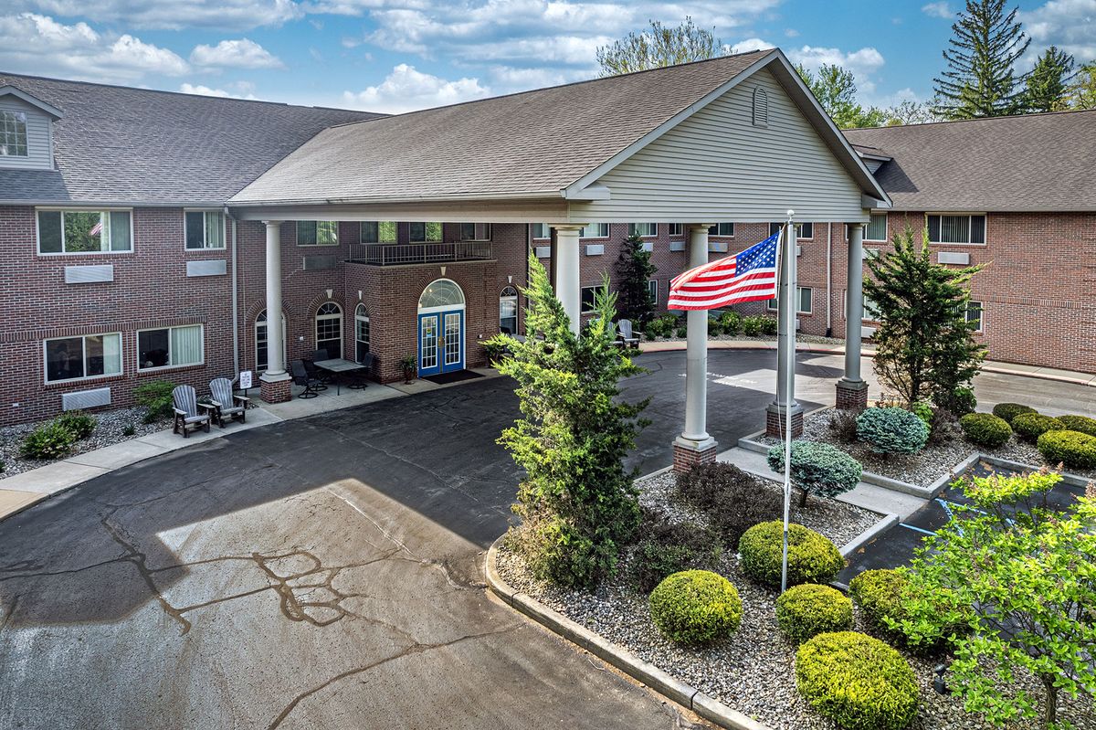 A building with an entrance, an American flag, and landscaped surroundings on a cloudy day.