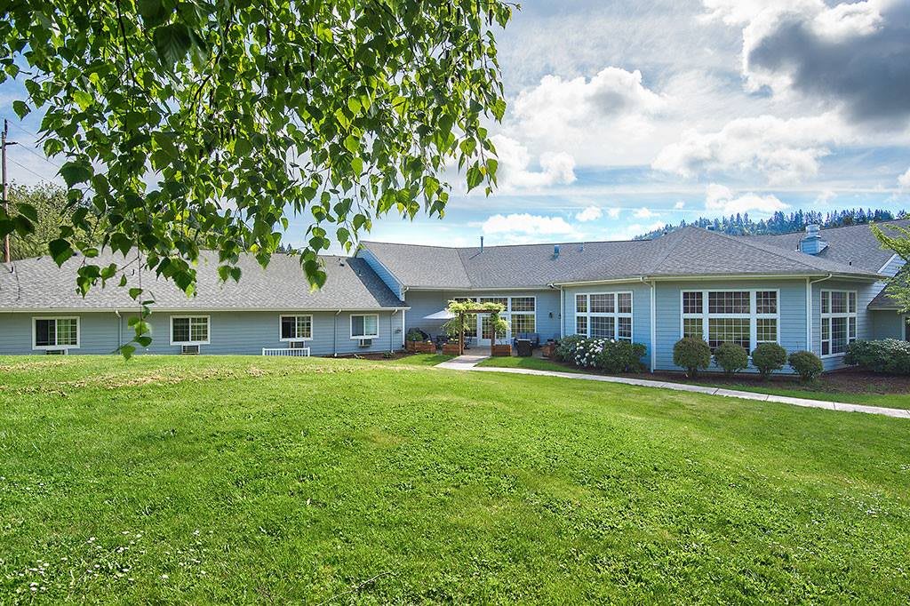 A spacious house with a large green lawn and trees under a partly cloudy sky.