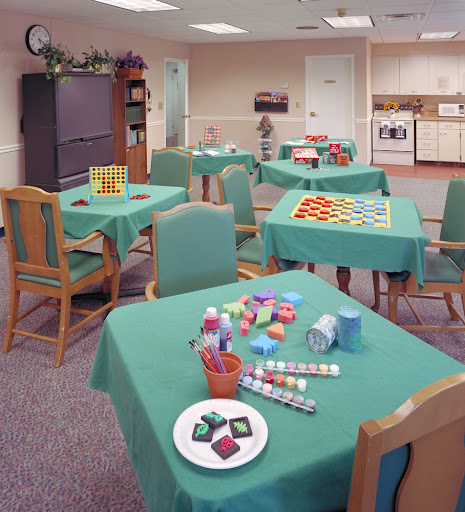 A vibrant activity area featuring tables with green tablecloths, chairs, and various colorful craft materials spread across the surfaces.