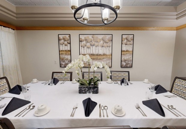 An elegantly set dining table with a white tablecloth, black napkins, and a centerpiece of orchids, beneath a modern chandelier and surrounded by artistic wall decor.