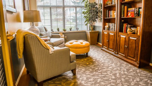 A cozy living room with armchairs, a bookshelf, and a window offering natural light.