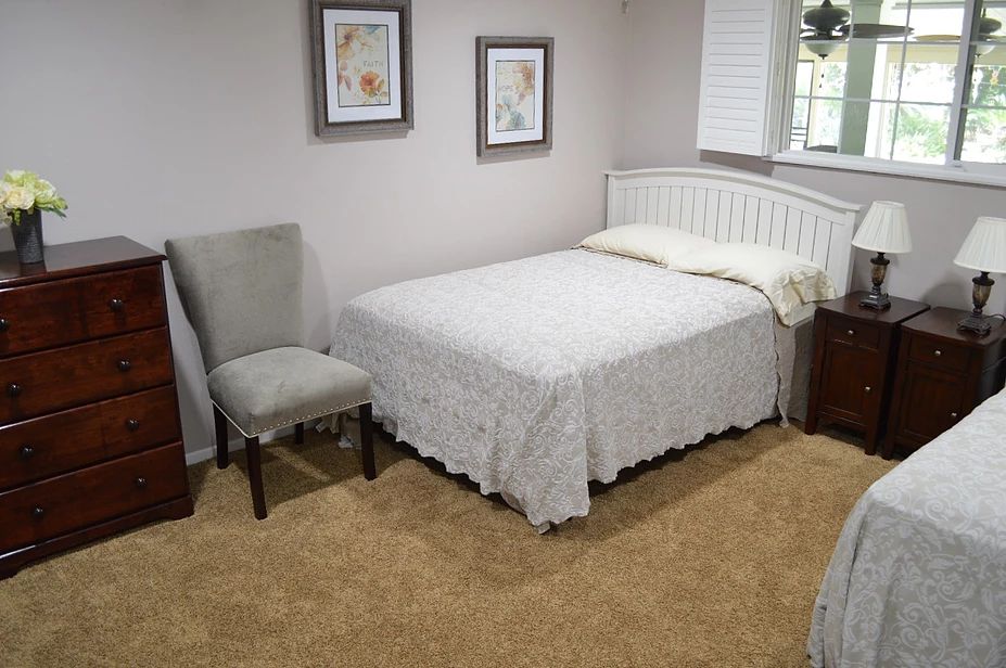 A cozy bedroom with a neatly made bed, a chair, and framed artwork on the walls.